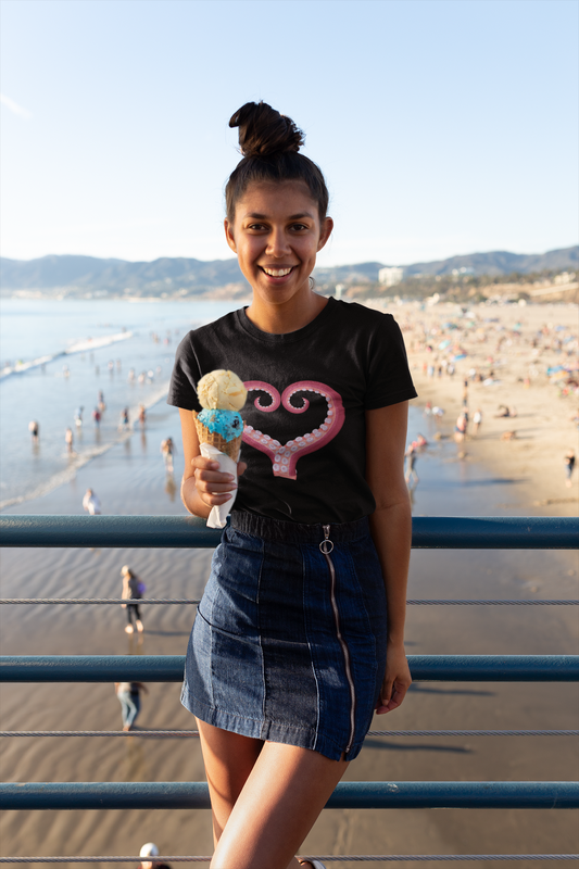 Young woman wearing a black t-shirt with a heart made out of octopus tentacles; she holds an ice cream cone and people are playing on the beach and in the ocean behind her